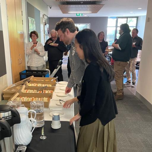 Picture of 2 students and a bunch of people talking and eating with the Workshop coffee break for Data Science and Statistics Lecture 2025