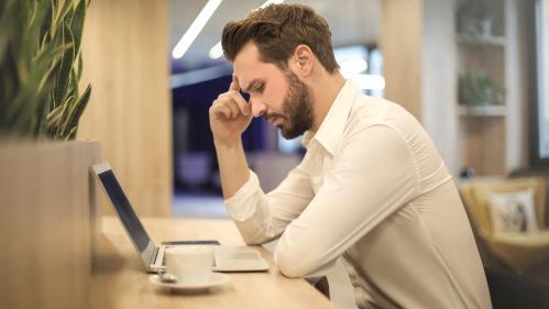 Photo of man sitting at a computer with his hand on his forehead