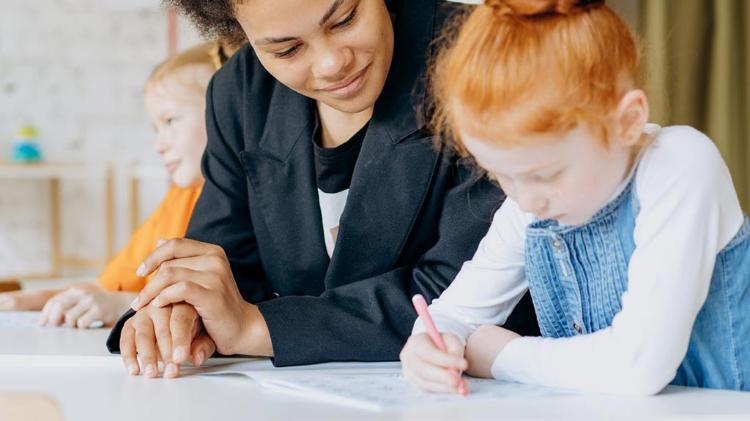 Preschool teacher sitting with student who is writing