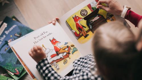 child sitting on lap of adult, having a story read to him