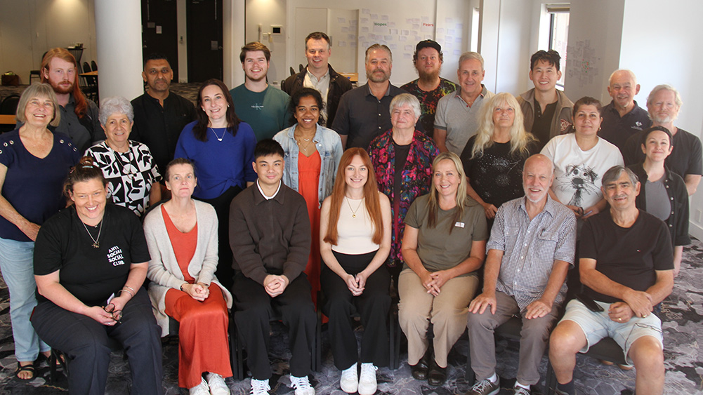Group photo of NSW Data Jury jurors gathered indoors, with approximately 25 participants arranged in seated and standing rows in a workshop or meeting space. Whiteboards and notes are visible in the background, reflecting the collaborative nature of the project.
