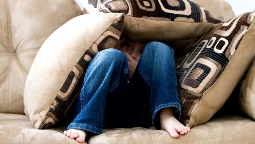 young cilld sitting under a pillow fort