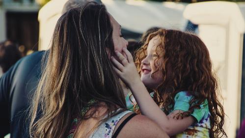 Photo of Mother holding daughter in her arms, with smiling daughter squeezing mothers face