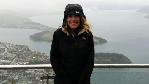 Loretta Jessop staning in the rain with a raincoat on with a beautiful backdrop of a river