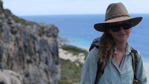 Photo of Lucy Farrier in an acubra standing on a mountain, with the ocean in the background