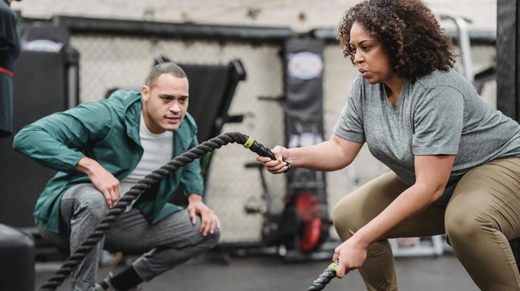 Woman works out with ropes while male trainer encourages her