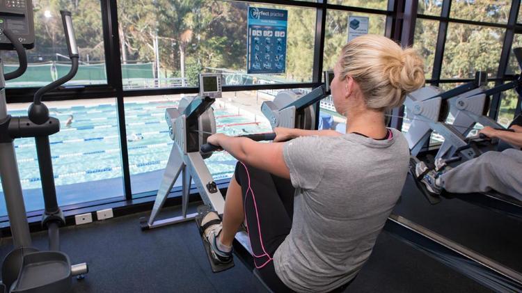 Female student using rowing machine at URAC looking out over pool