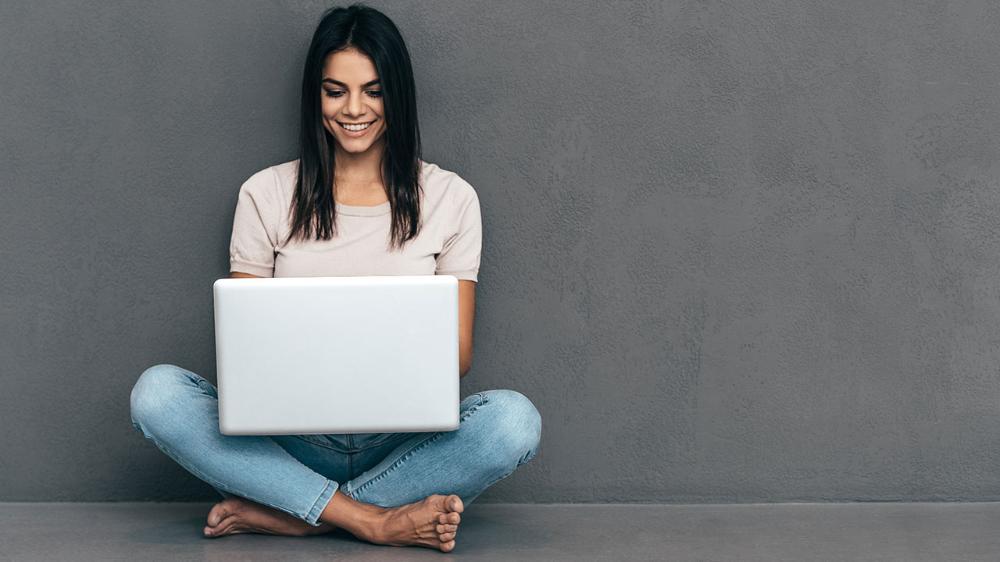 Lady sitting against grey wall with white laptop on lap