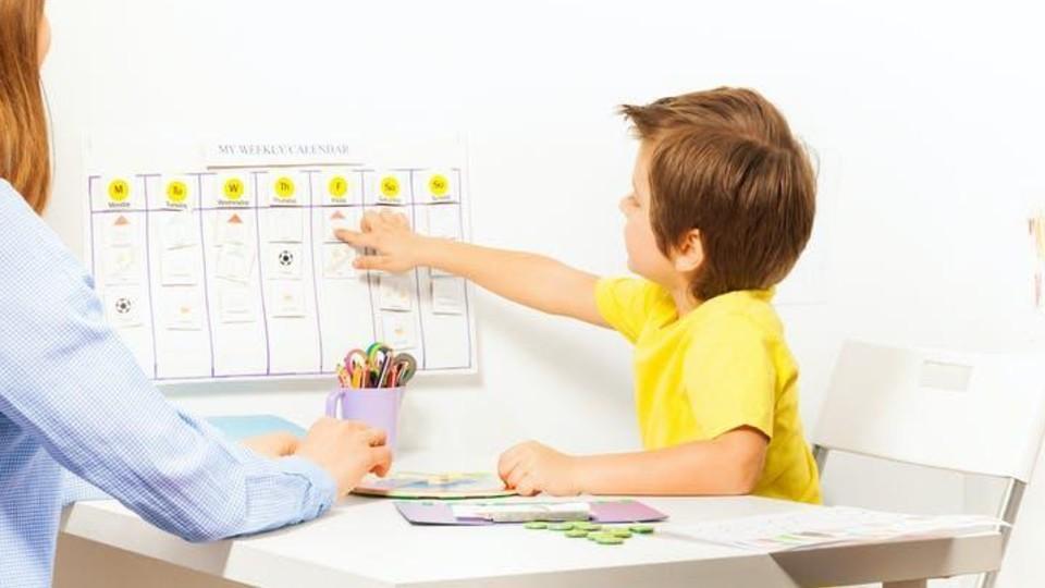 Young boy sitting at desk with mother, learning from home