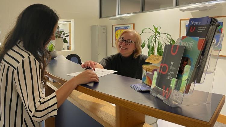 Client standing at the Northfields Psychology Clinic reception desk being served by a receptionist wearing a black workshirt.