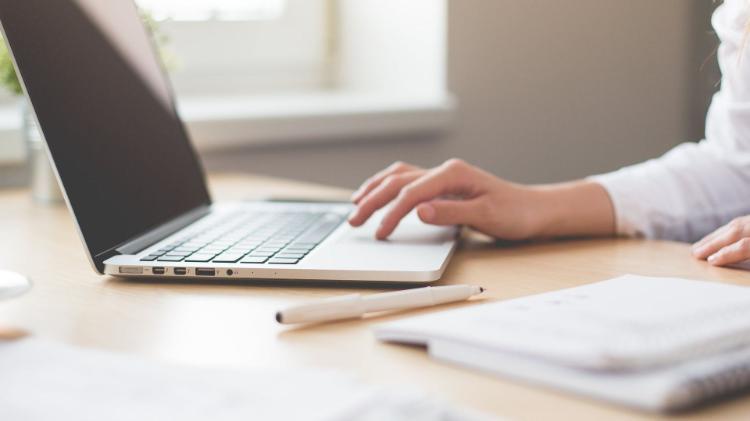 generic photo of lady sitting at desk on laptop with a pen and paper