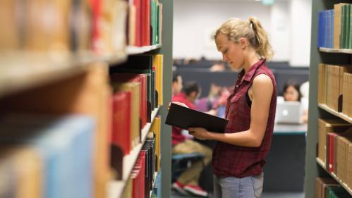 Student holding an open book in the Library