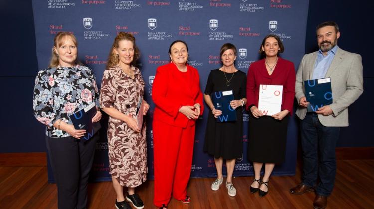 Library staff smiling and holding their recognition certificates beside UOW VC, Patricia Davidson