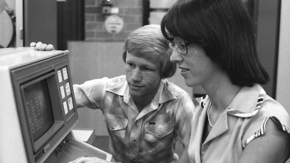 Black and white photograph of two students at a computer terminal in the 1970s