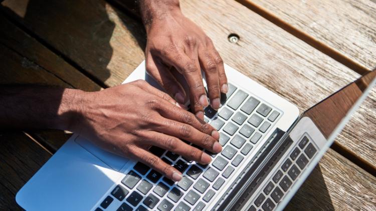 Person typing on laptop computer outdoors.