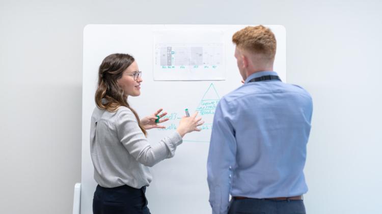 Two people standing near whiteboard talking.