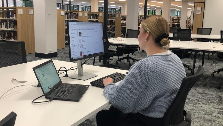 Student seated facing a monitor and studying with laptop connected to monitor.