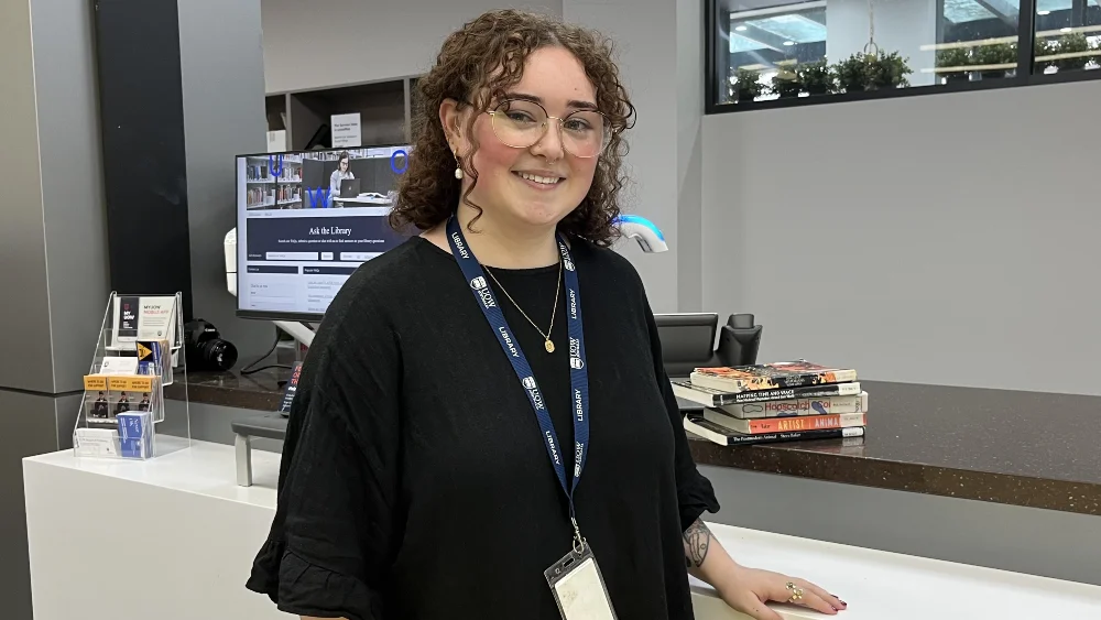 Library staff member smiling standing near client services desk