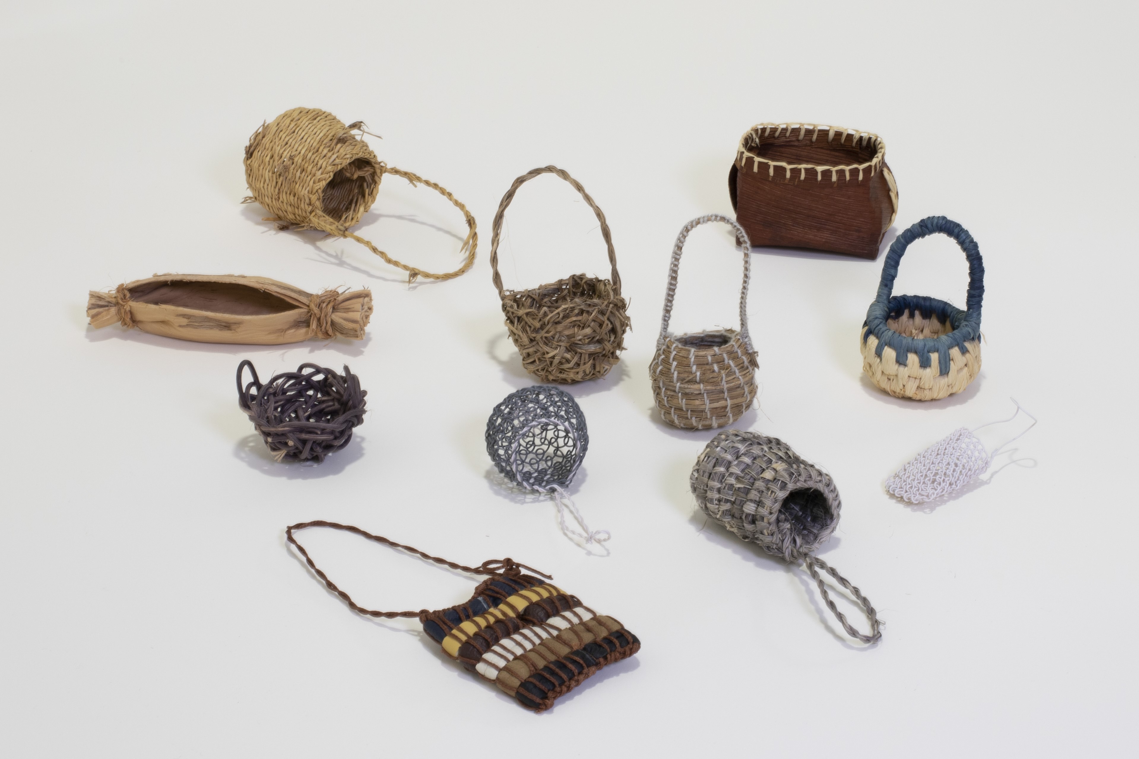 11 miniature woven baskets of various shapes, fibres and colours.