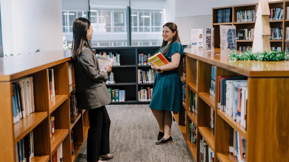 Two students standing next to bookshelves smiling.