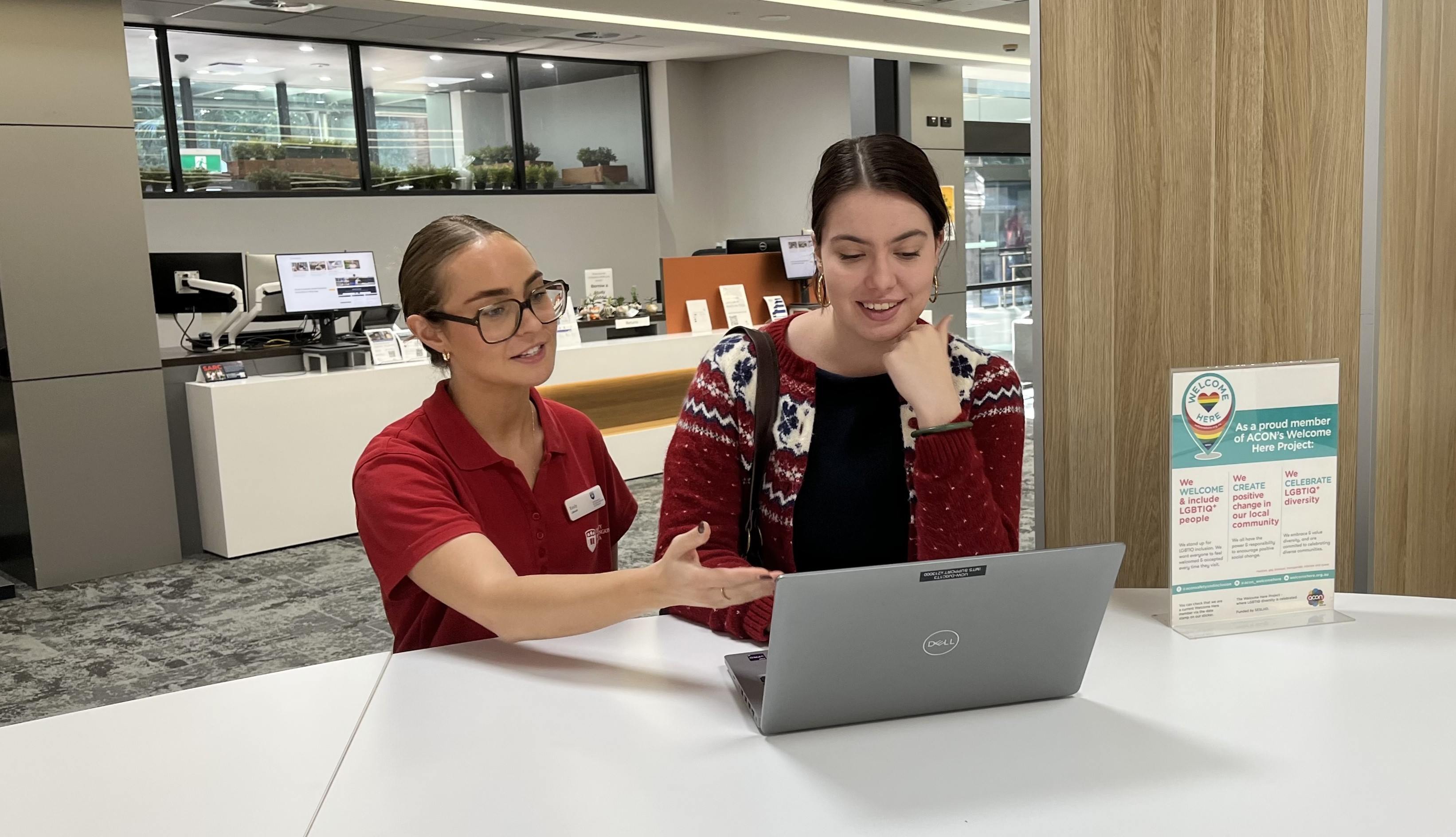 Two people standing at a desk with a laptop talking.