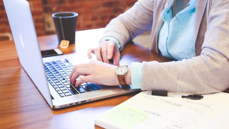 Person at a laptop with an open book and coffee cup beside them