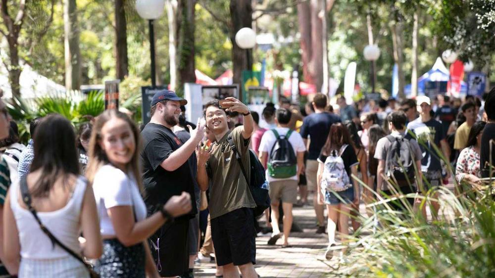 Two students taking selfies on campus in front of a crowd
