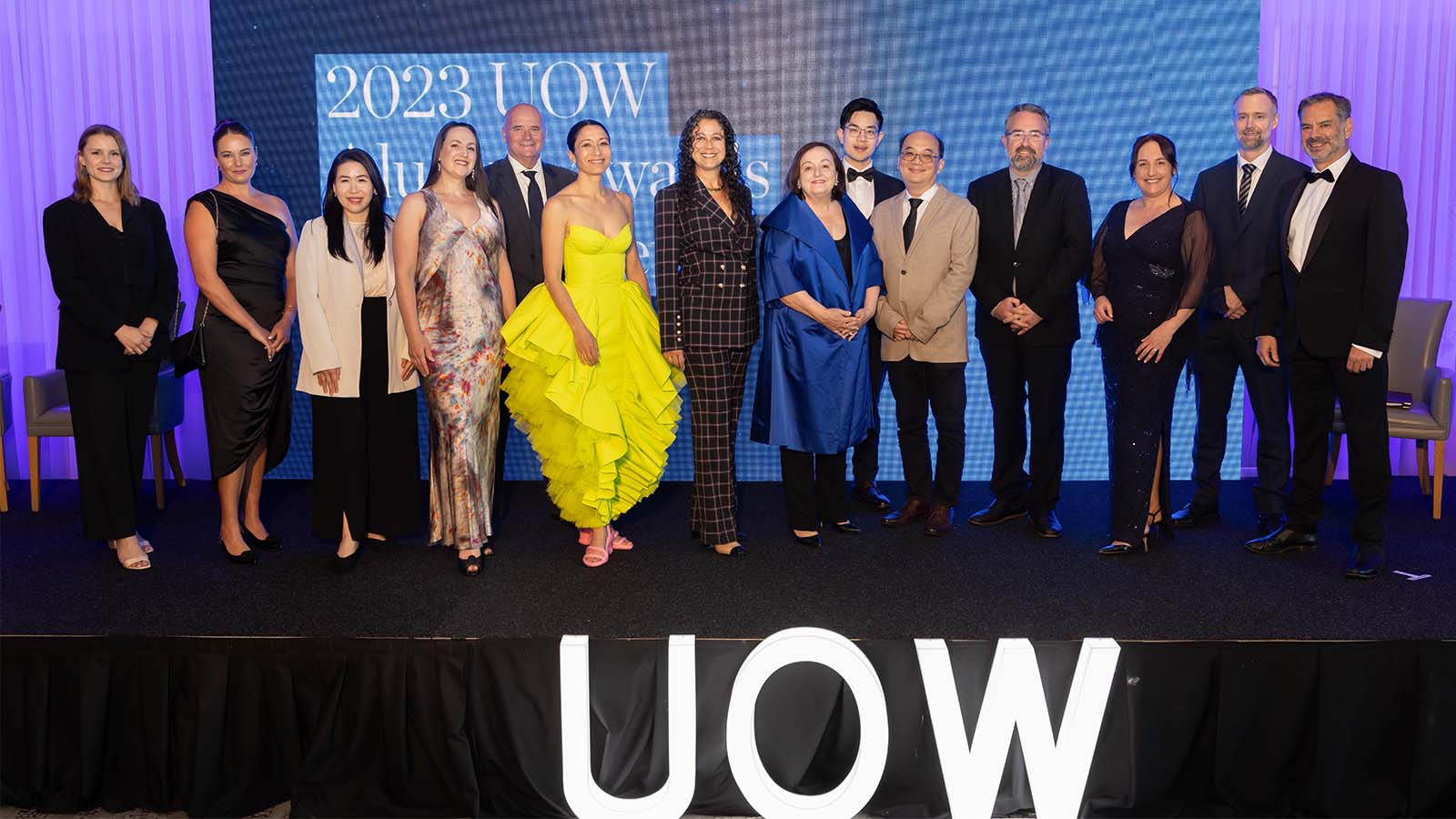 A group of people standing in front of a UOW wall
