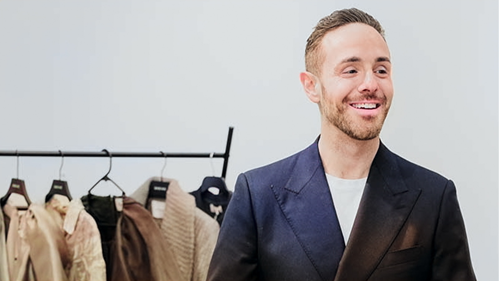 A man is wearing a suit, standing in front of a clothes rack
