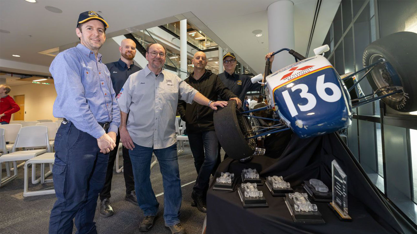 A group of men are crowded around a small motorsport car