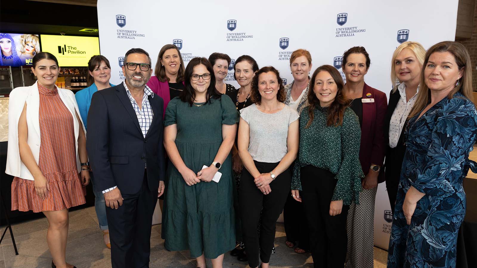 A group of people standing in front of a white UOW media wall