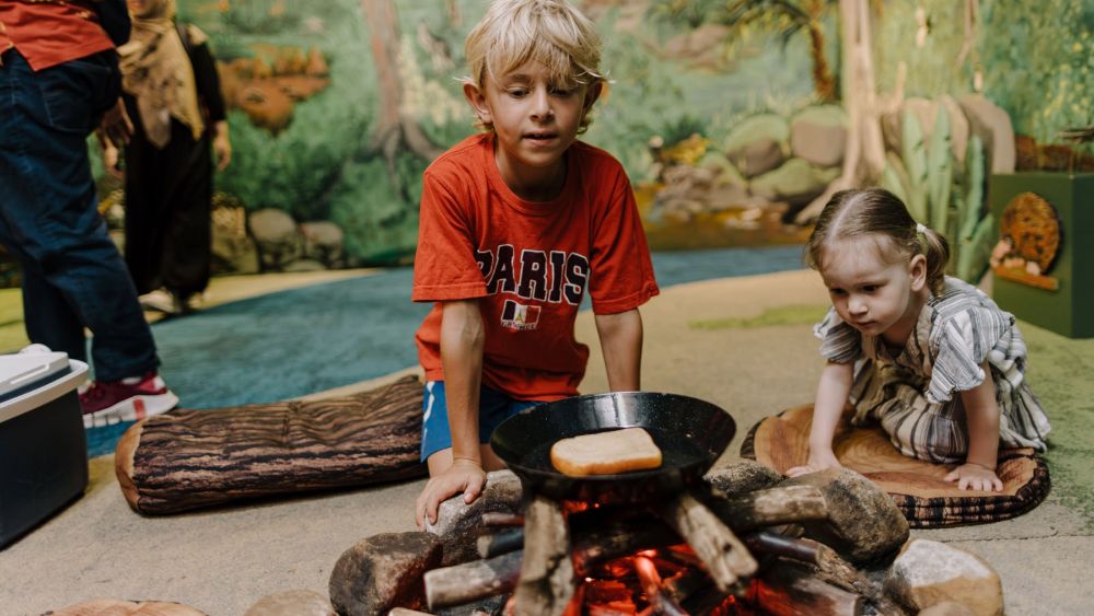 Two young children playing in a make-believe camping area with a pretend camp fire.