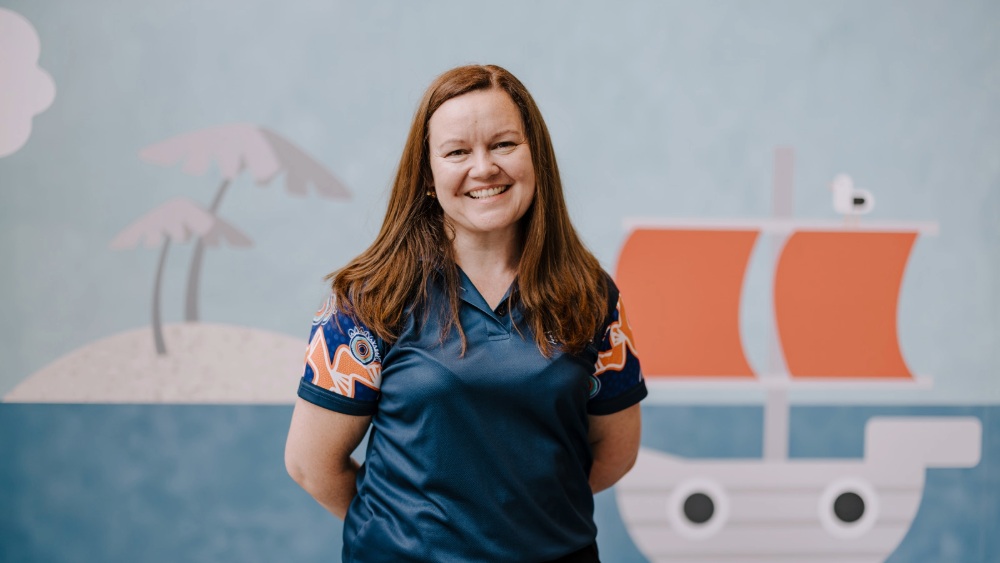 Smiling woman wearing an Early Start polo shirt stands in front of an ocean mural