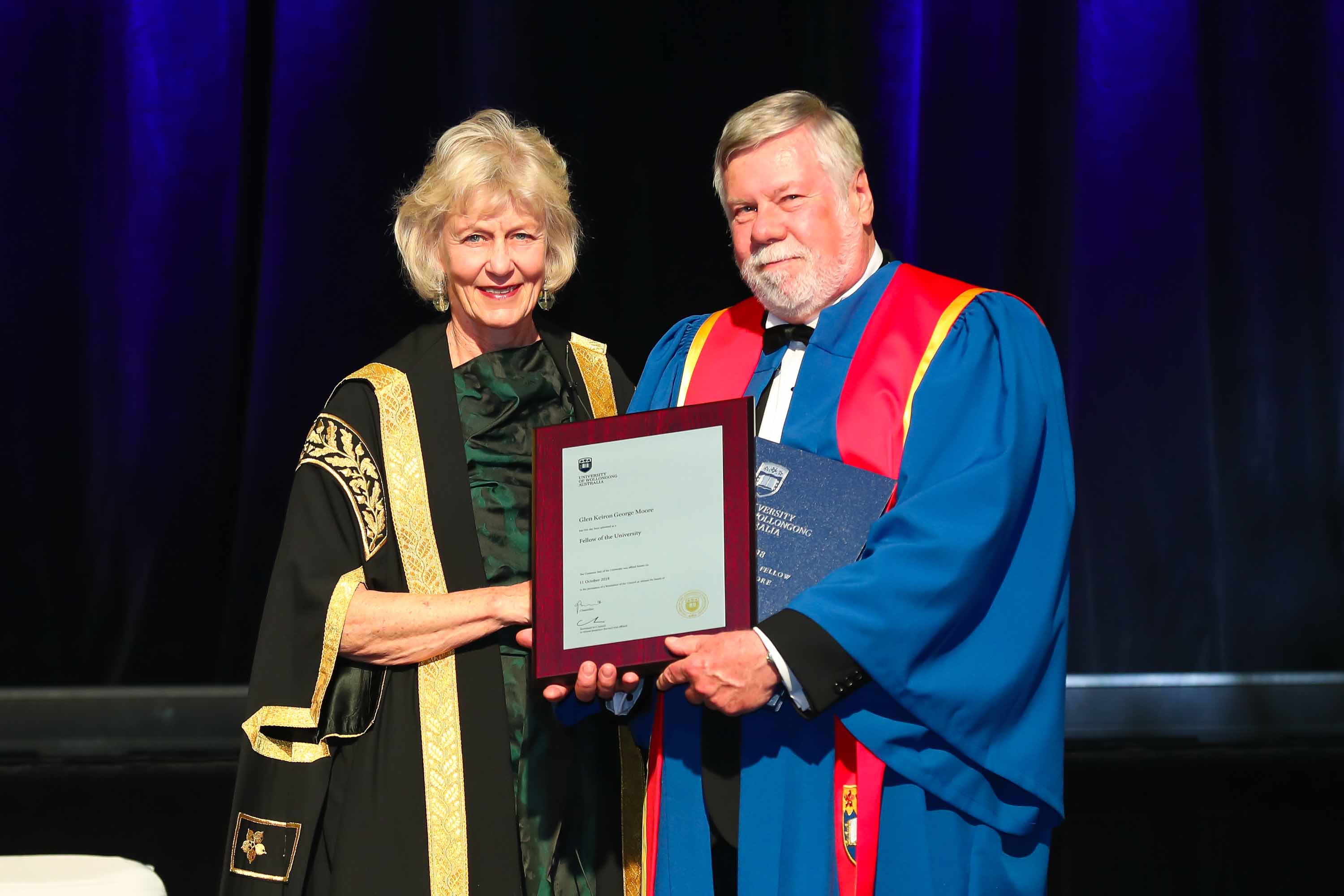Dressed in ceremonial robes, a woman presents a man with a plaque.