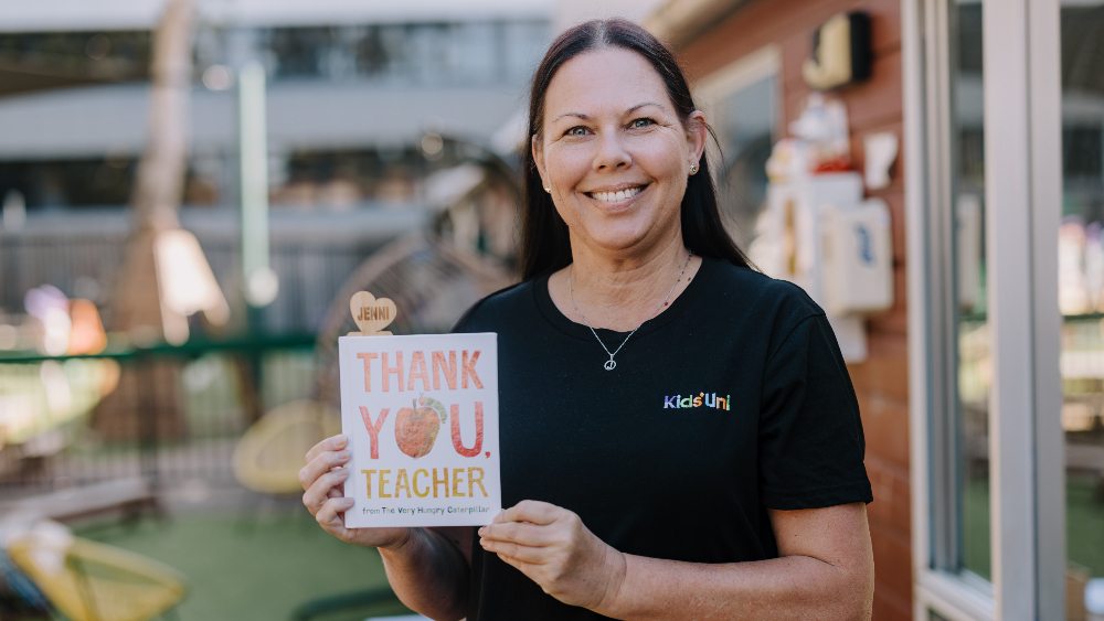 Kids' Uni educator Jenni Smith smiles at the camera while holding a book titled Thank You Teacher, with a personalised bookmark with her name. Photo: Michael Gray
