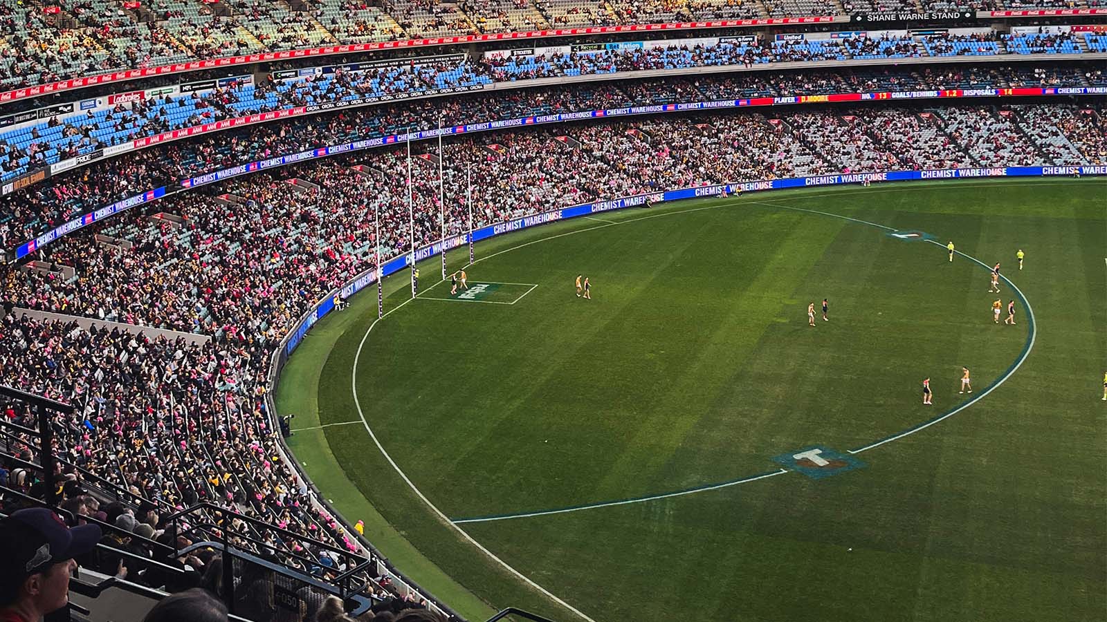 A wide view of the Melbourne Cricket Ground during an AFL match, showing players on the field and a large crowd in the stands.