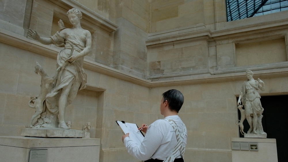 Standing in front of two sculptures, an artist sketches.