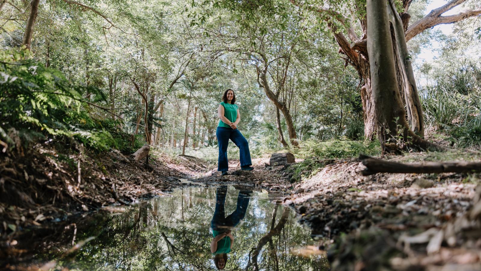 Associate Professor Sonia Graham standing above a creek with her reflection in the water below. Photo: Michael Gray