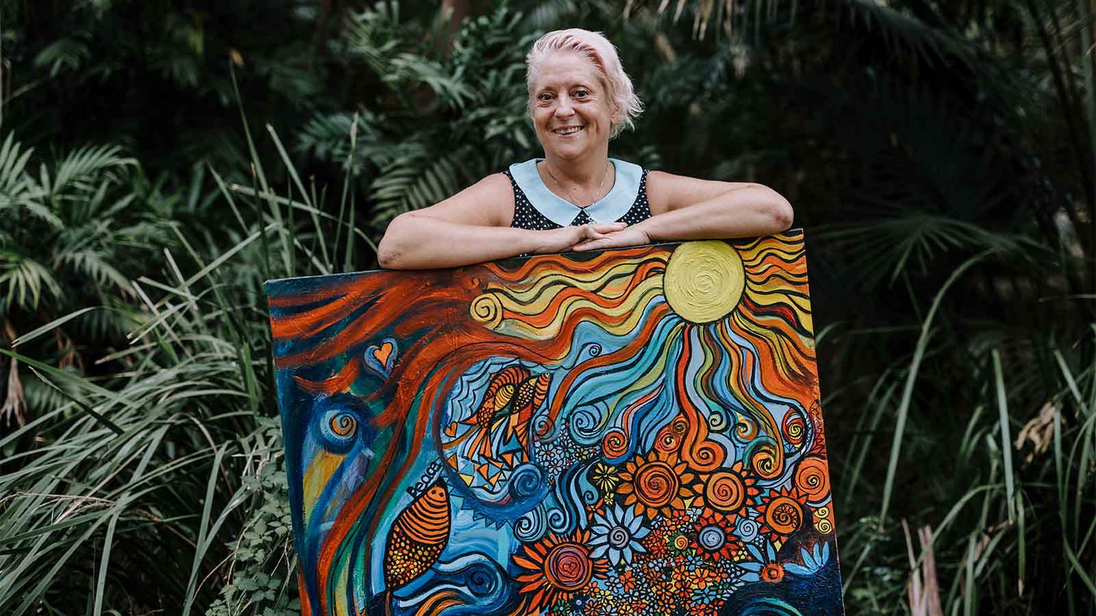 A woman has her arms leant over a large canvas abstract painting of a woman.