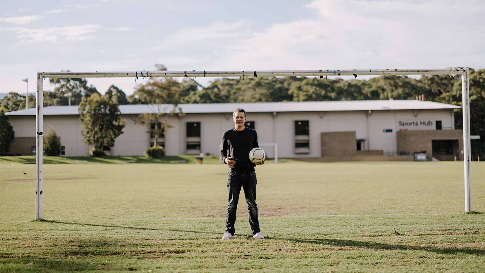 A man is standing on a soccer field in front of a goal post, holding a soccer ball