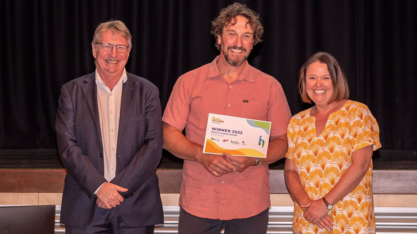A man is holding an award, standing in between a man and a woman