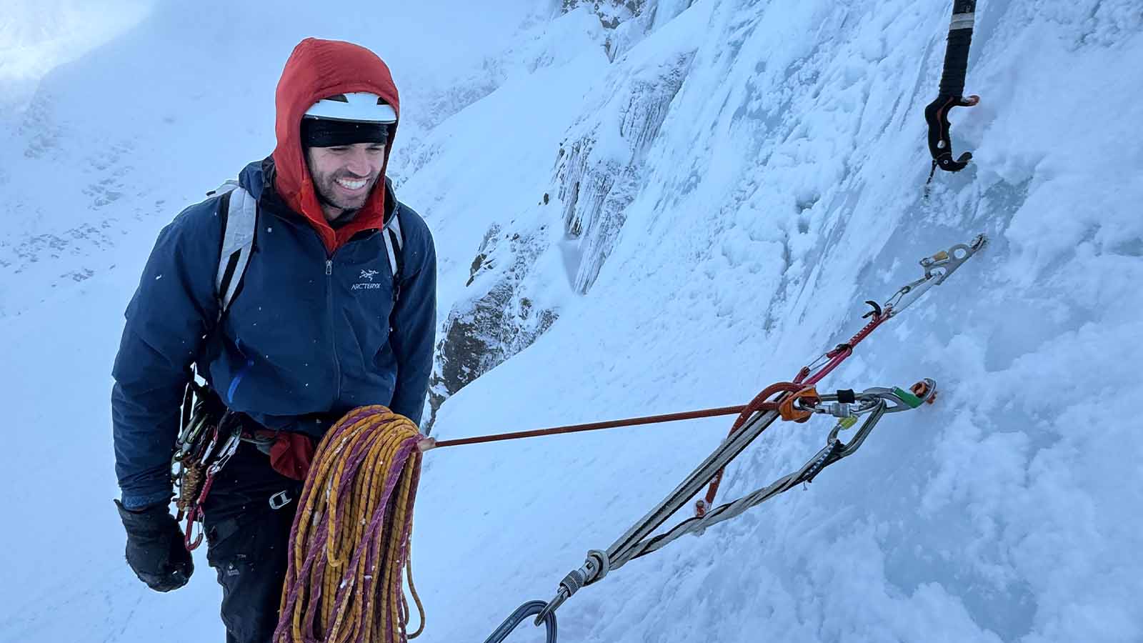 A man is scaling an icy cliff with rockclimbing ropes