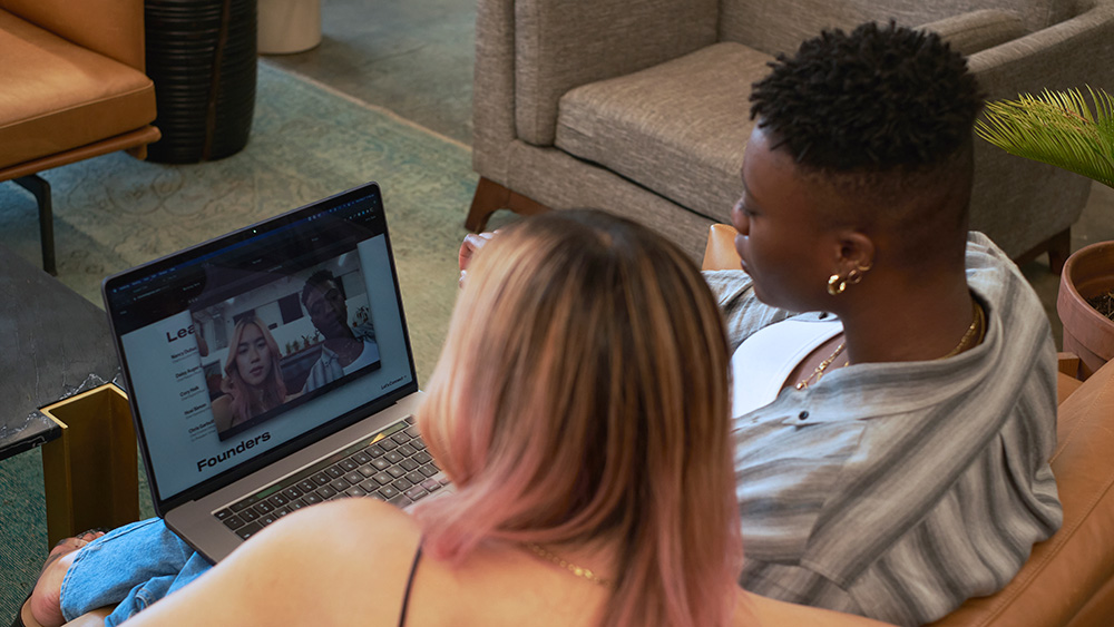 A non-binary person and transfeminine person on a video call in an office