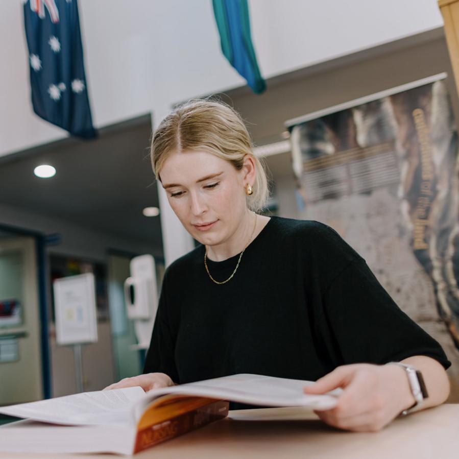 A blonde woman in a black tshirt is studying a textbook at UOW Eurobodalla campus