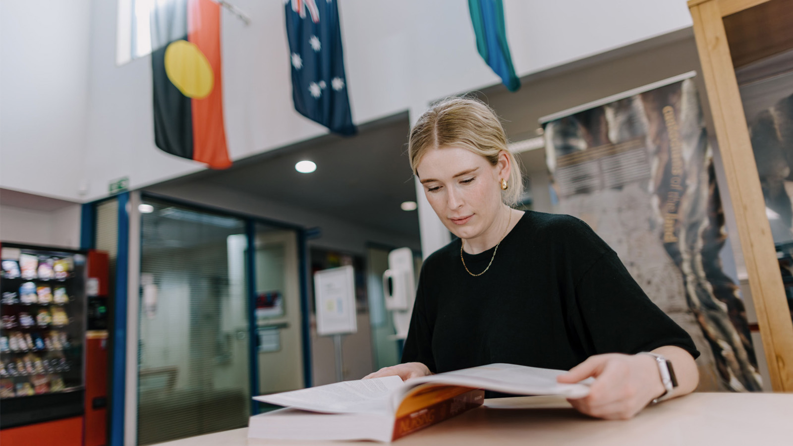 A blonde woman in a black tshirt is studying a textbook at UOW Eurobodalla campus