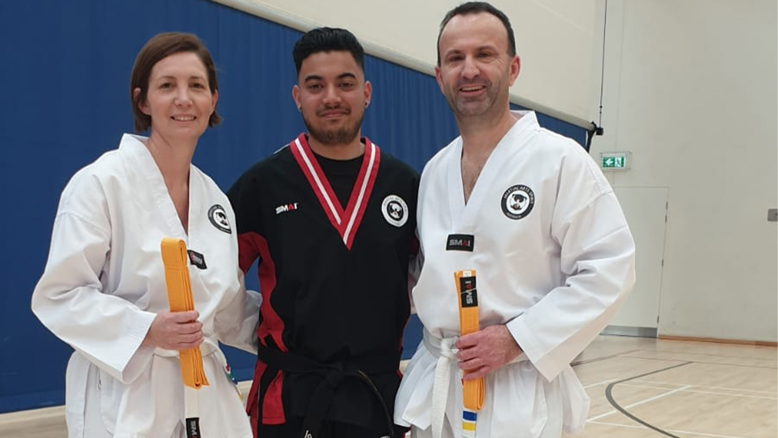 A woman and two men are standing on a martial arts mat in uniform
