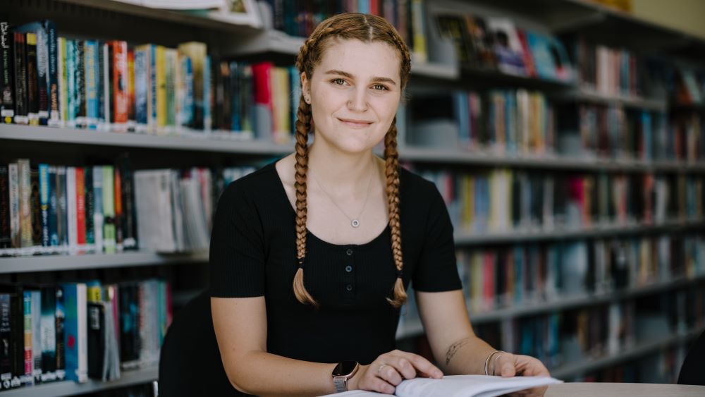 Female student sitting at desk with bookshelf behind her