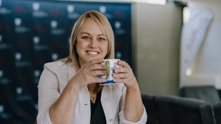 Female student sitting at desk holding coffee cup, smiling at the camera