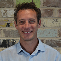 David Malins smiling at camera with a brickwall background