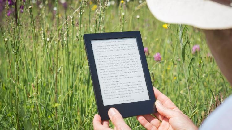 A man wearing a hat holding an ebook with a grassy background